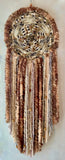 Dreamcatcher is made by Sarah Moody with a multi-color blend doily made by Vicki Portch. This beauty has five different high-quality yarns in shades of black, brown, tan and cream. The center Jaguar head is made from brass with inlaid golden rhinestones. Scattered wooden and miscellaneous beads are stitched and strung throughout the piece. This is definitely a power piece. Made with focus, attention to detail, and a whole lot of love!  Measurements: 43" in length and 15-16" inches wide